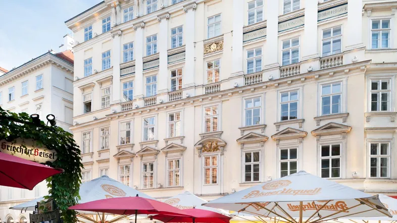 Klassisches Gebäude mit eleganter Fassade und einem belebten Straßencafé im Vordergrund.
