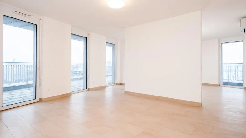 Helles, leeres Wohnzimmer mit großen Fenstertüren und hellem Fliesenboden.