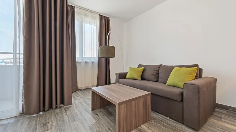 Helles Wohnzimmer mit beigem Sofa, Holztisch und Zugang zu einem Balkon.