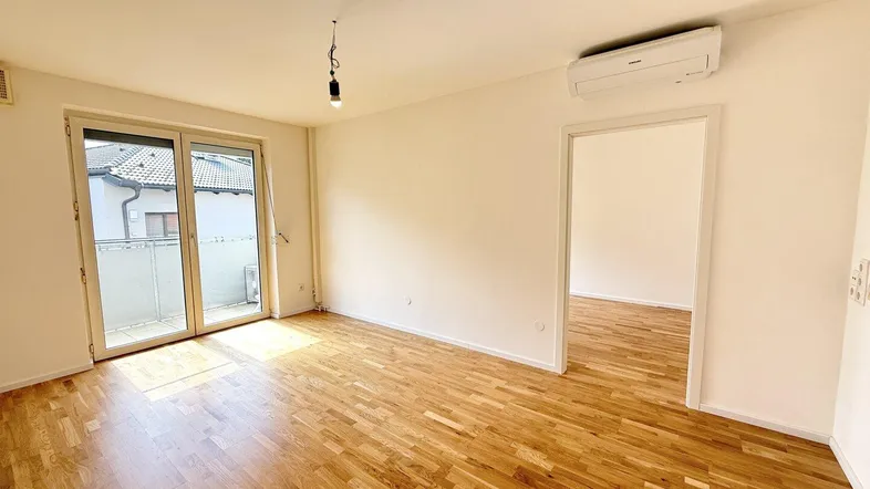 Helles Zimmer mit Parkettboden, Zugang zum Balkon und Klimaanlage an der Wand.