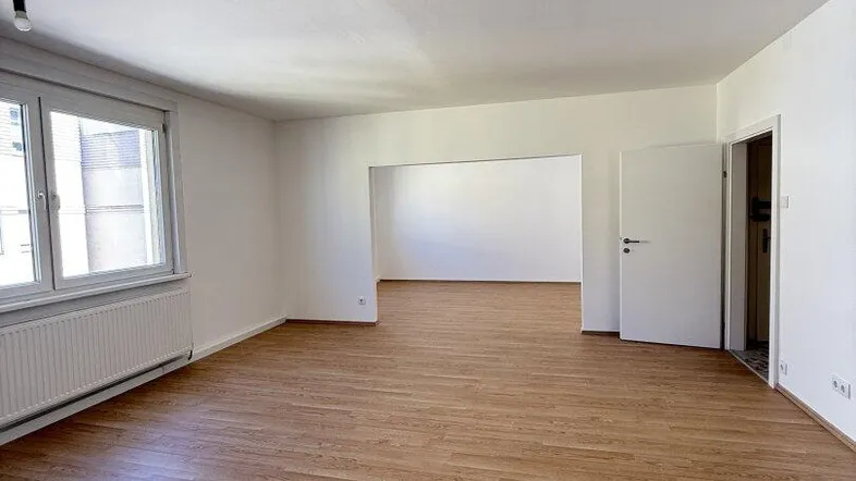 Geräumiges und helles Wohnzimmer mit Laminatboden und großen Fenstern, bereit zur individuellen Gestaltung.