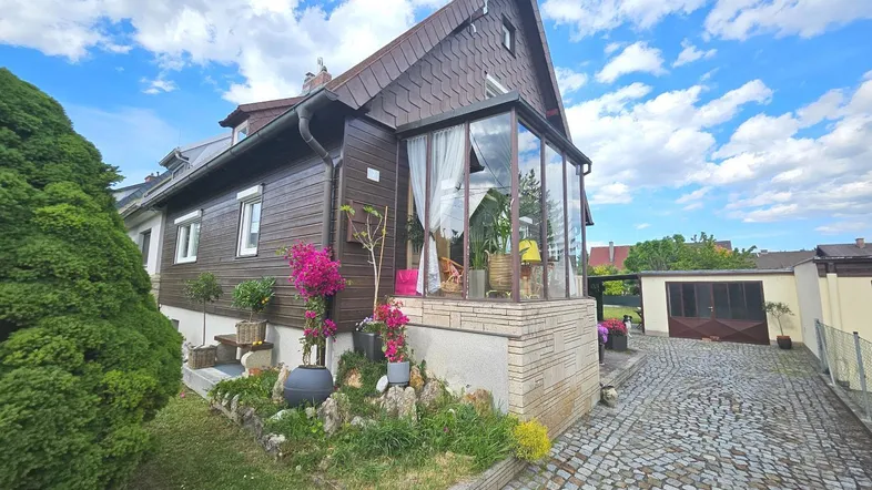 Ansicht des Hauses von der Seite mit einem verglasten Wintergarten und gepflasterter Auffahrt.