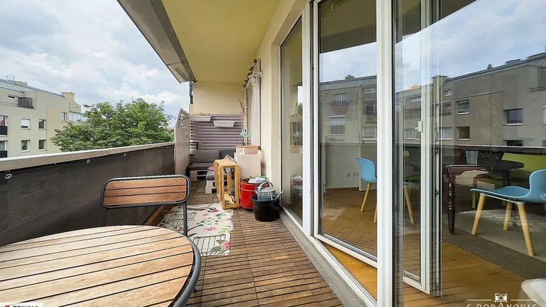 Geräumiger Balkon mit Holzboden und Sitzgelegenheiten, bietet einen Blick auf die umliegenden Gebäude.