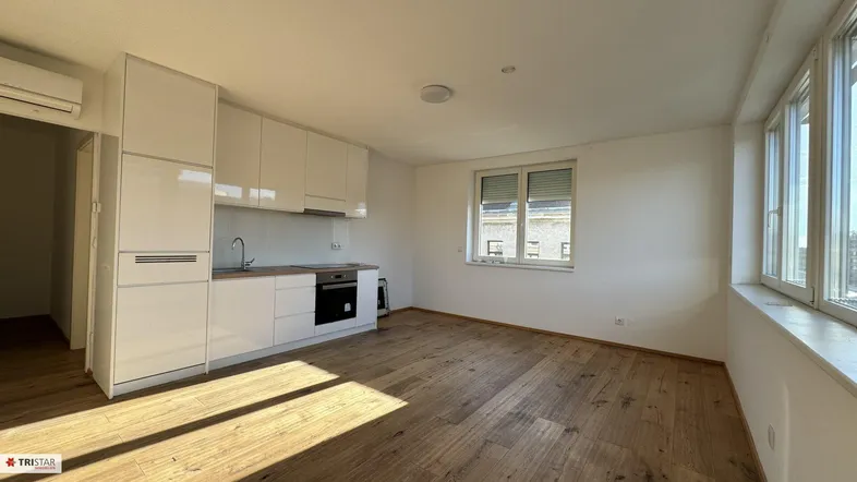 Helles Wohnzimmer mit integrierter weißer Küche, Holzboden und großen Fenstern.