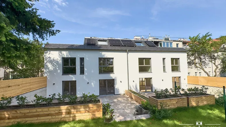 Moderne Doppelhaushälfte mit weißer Fassade, Garten und Solaranlage auf dem Dach.