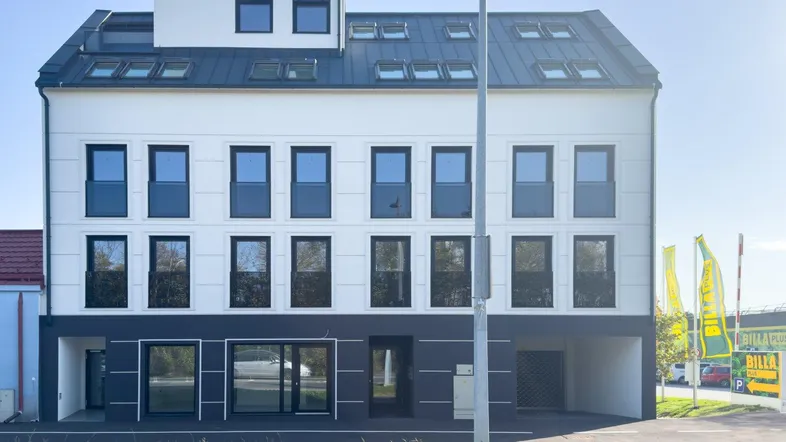 Modernes Mehrfamilienhaus mit weißer Fassade, dunklen Fenstern und einem Satteldach mit Gauben.