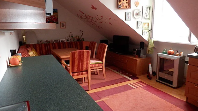 Gemütlicher Wohn-Essbereich im Dachgeschoss mit Holztisch, Sitzbank und Fernsehmöbeln unter der Dachschräge.