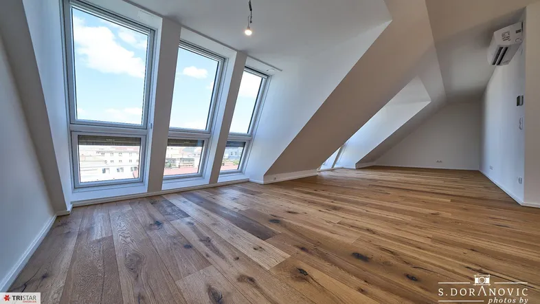Geräumiger Dachgeschossraum mit großen Fenstern, Holzboden und Klimaanlage, ideal für Wohnzwecke.