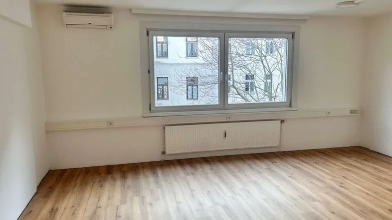 Heller Büroraum mit modernem Laminatboden, großen Fenstern und Klimaanlage für angenehmes Raumklima.