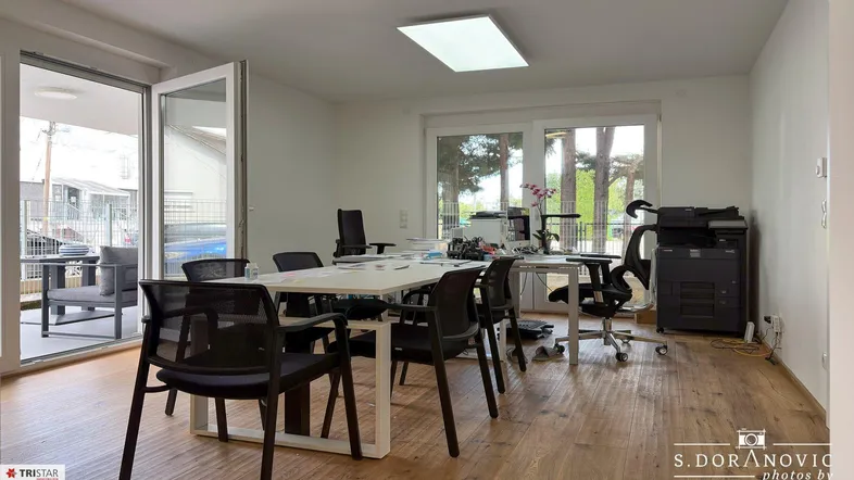 Helles Büro mit Holzboden, großen Fenstern und Zugang zu einer Terrasse.