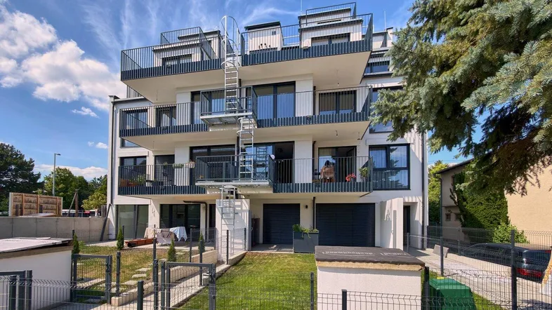 Modernes Mehrfamilienhaus mit mehreren Balkonen und einer Außentreppe unter blauem Himmel.