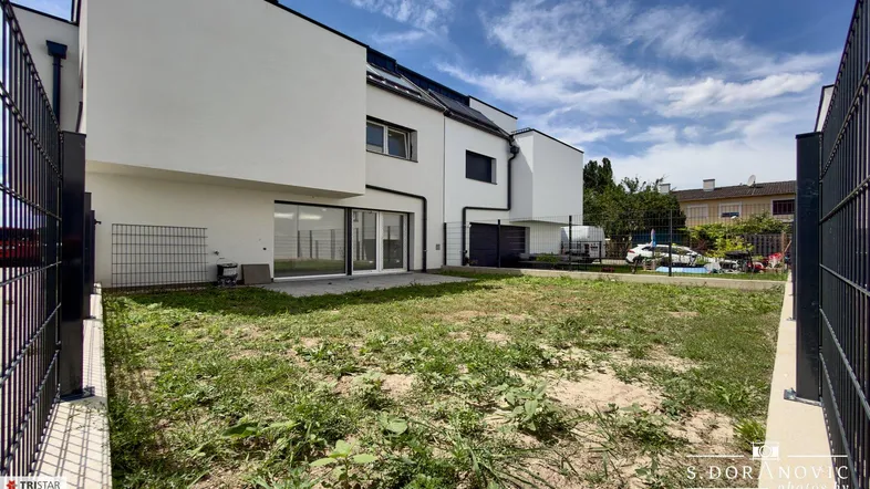 Hinterer Gartenbereich eines modernen Neubaus mit Rasenfläche und großen Glasfronten.