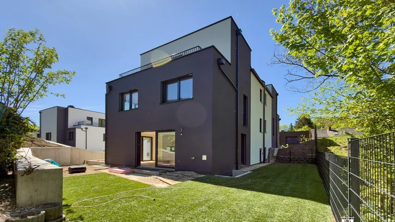 Modernes Reihenhaus mit dunkler Fassade und privatem Gartenbereich unter blauem Himmel.