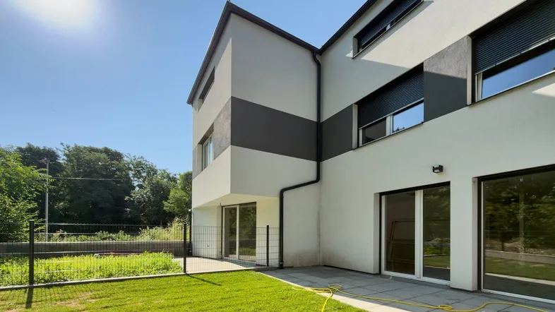 Moderne Hausfassade mit weißer und grauer Farbgebung, angrenzender Terrasse und kleinem Gartenbereich.