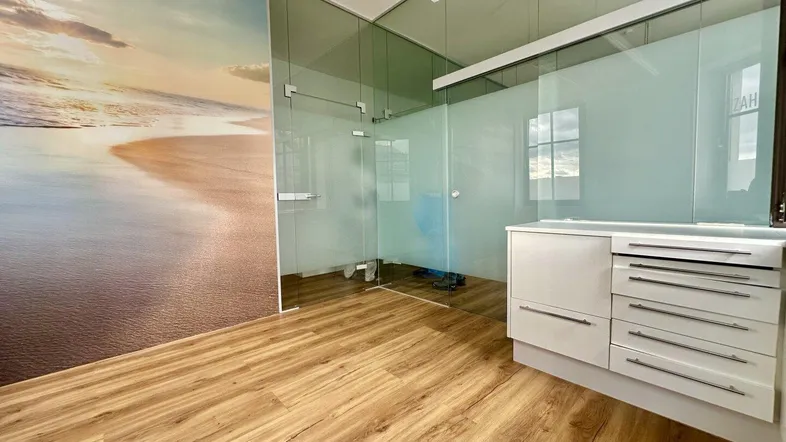 Moderner Bürobereich mit Holzboden, Glaswänden und einer Strandtapete, bietet viel Tageslicht.