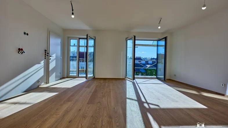 Helles Wohnzimmer mit Holzboden und Zugang zu zwei Balkonen, durchflutet von Sonnenlicht.