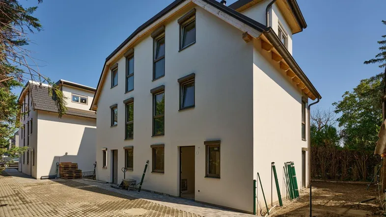 Neubau-Doppelhaushälfte mit weißer Fassade und sichtbaren Bauarbeiten im Außenbereich.