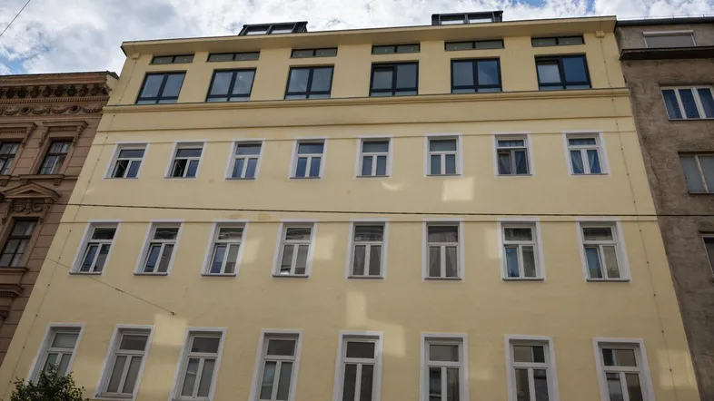 Fassade eines Mehrfamilienhauses in hellem Gelb mit vielen Fenstern und Dachausbau.