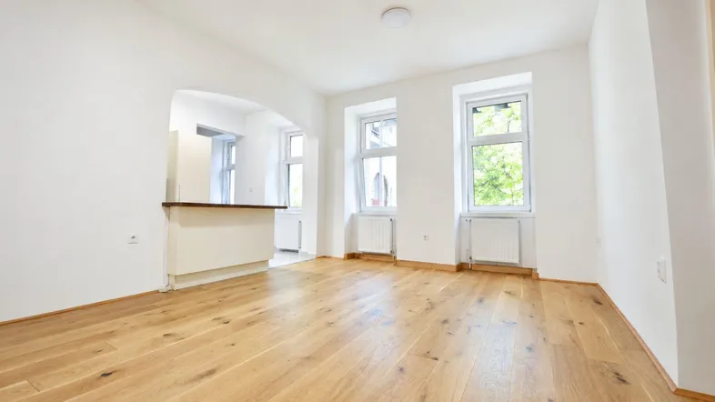 Helles Wohnzimmer mit neuem Parkettboden und Zugang zu einem offenen Küchenbereich.