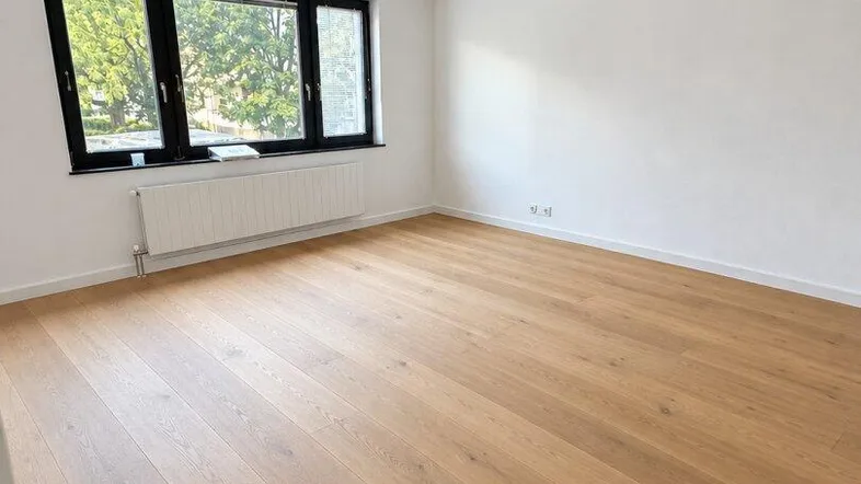 Helles Zimmer mit Holzfußboden und Fenster mit Blick ins Grüne, bereit zur Einrichtung.