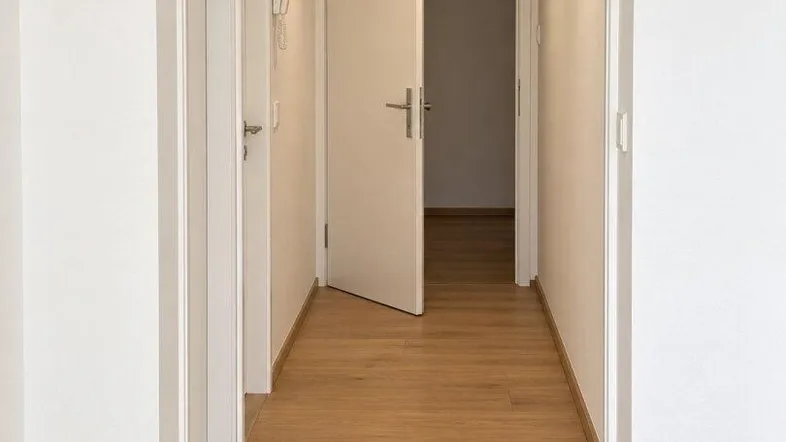 Heller Flur mit Holzboden und weißen Wänden, der zu weiteren Räumen führt.