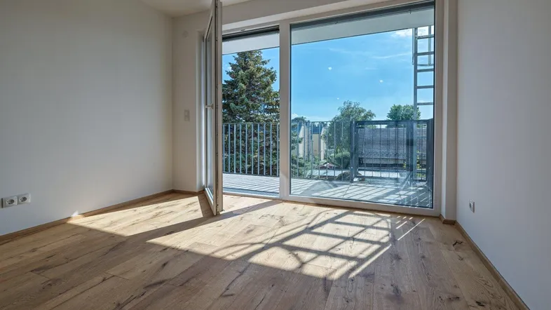 Helles Zimmer mit Holzboden und Zugang zu einem Balkon, bietet viel natürliches Licht.