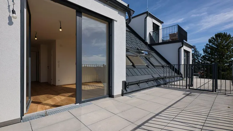 Große Dachterrasse mit Fliesenboden und Zugang zu einem hellen Innenraum.