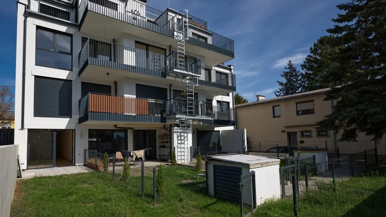 Modernes Mehrfamilienhaus mit mehreren Balkonen, einer kleinen Grünfläche und einem Schuppen im Gartenbereich.