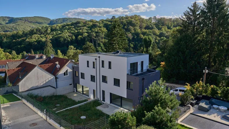 Moderne Wohnanlage mit Flachdach und umliegender grüner Hügellandschaft unter blauem Himmel.