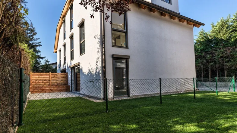 Modernes Einfamilienhaus mit weißer Fassade und gepflegtem Rasen im sonnigen Gartenbereich.