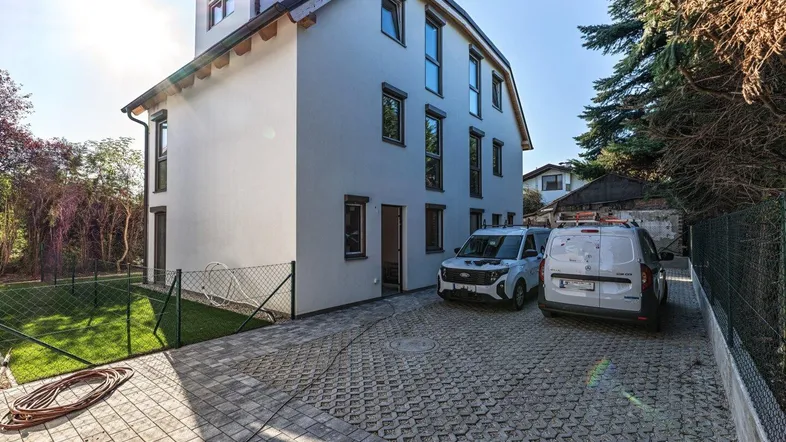 Modernes Einfamilienhaus mit weißer Fassade, gepflasterter Einfahrt und angrenzendem Gartenbereich.