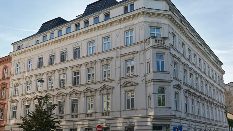 Elegantes Eckgebäude mit klassischer Fassade und modernem Dachausbau in urbaner Umgebung.