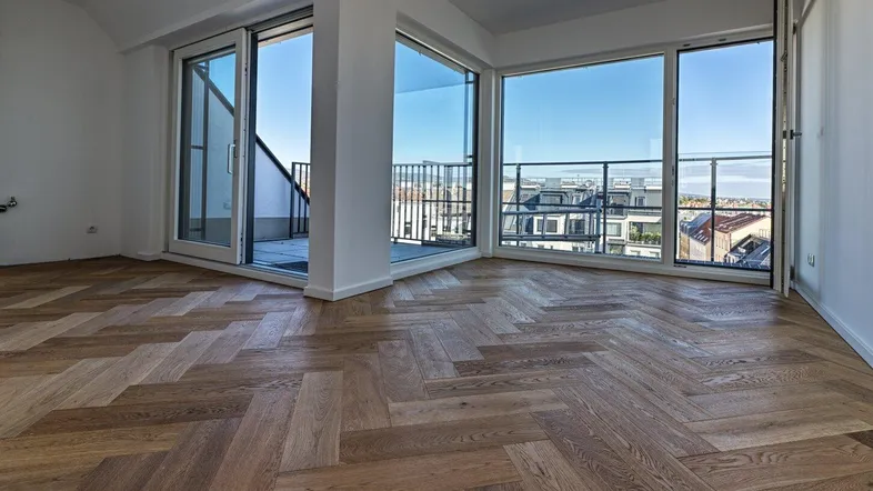 Helles Zimmer mit Fischgrätparkett und großen Fenstern, die Zugang zu einem Balkon mit Stadtblick bieten.