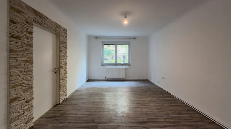 Helles Zimmer mit Laminatboden und dekorativer Steinwand am Türrahmen, bereit zur individuellen Gestaltung.