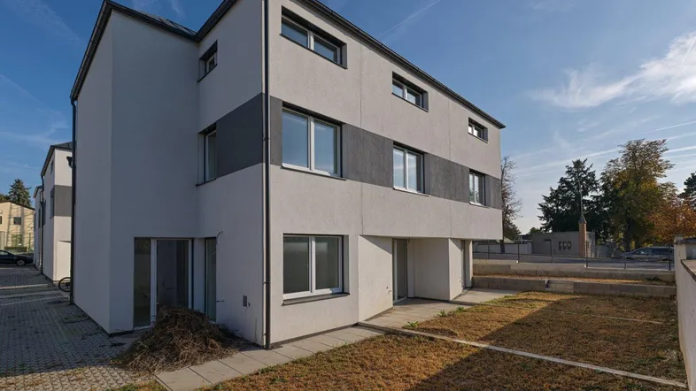 Modernes Reihenhaus mit kleiner Gartenfläche und Terrasse im Bauzustand unter blauem Himmel.