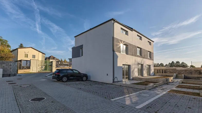 Modernes Reihenhaus mit heller Fassade und Parkplätzen im Freien unter blauem Himmel.