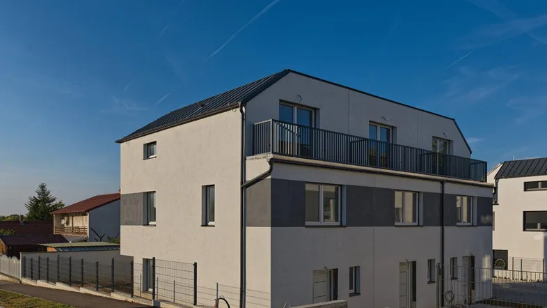 Modernes Mehrfamilienhaus mit weißer und grauer Fassade sowie einem Balkon im Obergeschoss.