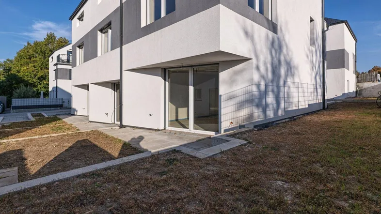 Moderne Reihenhausfassade mit weiß-grauem Anstrich und einer kleinen Terrasse im Rohbauzustand.