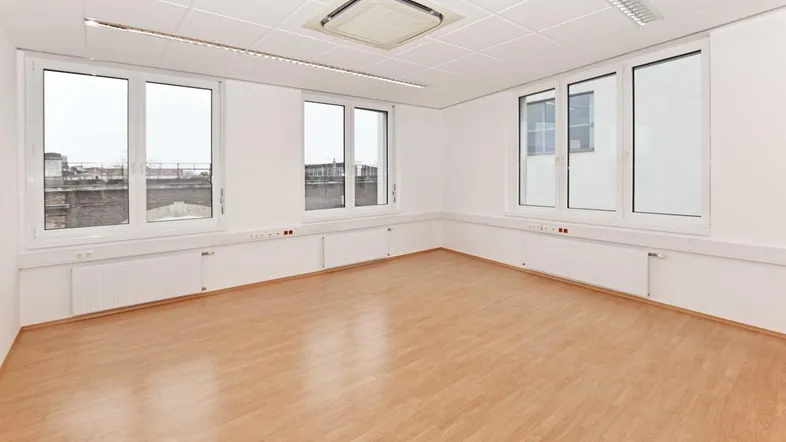 Helles und geräumiges Büro mit großen Fenstern, Klimaanlage und hellem Laminatboden, ideal für verschiedene Nutzungen.