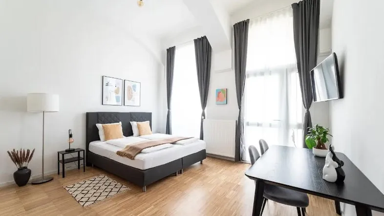 Helles Schlafzimmer mit Doppelbett, Esstisch und hohen Fenstern, modern eingerichtet.