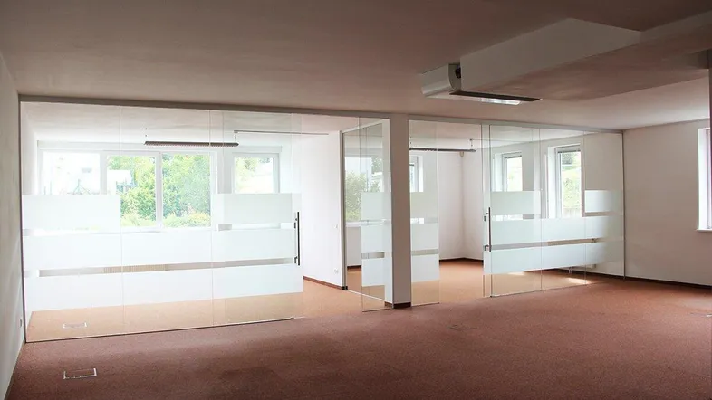 Heller Büroraum mit Teppichboden und modernen Glasabtrennungen, die natürliches Licht hereinlassen.