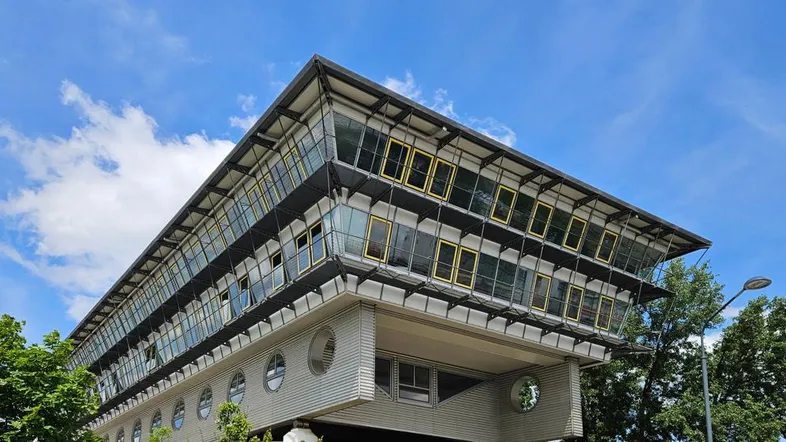 Modernes Gebäude mit markanter Glasfassade und großen Fenstern unter blauem Himmel mit Wolken.