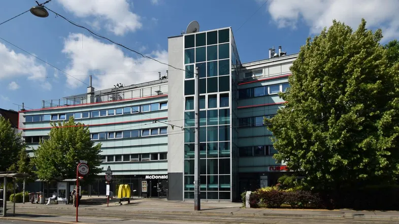 Modernes Geschäftsgebäude mit großen Fenstern, einem McDonald's im Erdgeschoss und viel Grün in der Umgebung.