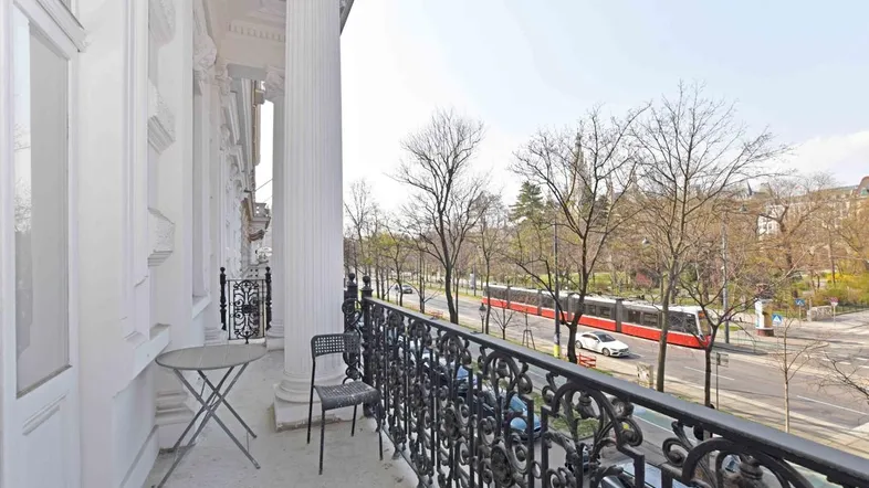 Geräumiger Balkon mit schmiedeeisernem Geländer und Blick auf die belebte Stadtstraße mit Straßenbahn.