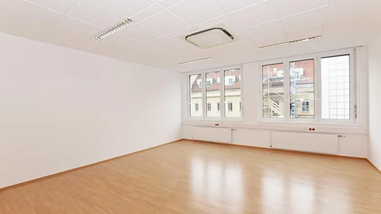 Heller, leerer Büroraum mit Laminatboden, weißen Wänden und Deckenklimaanlage.