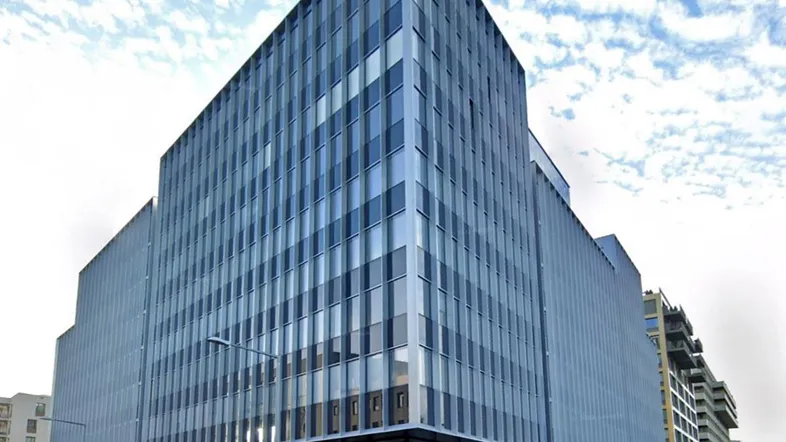 Modernes Bürogebäude mit markanter Glasfassade und klaren Linien unter bewölktem Himmel.