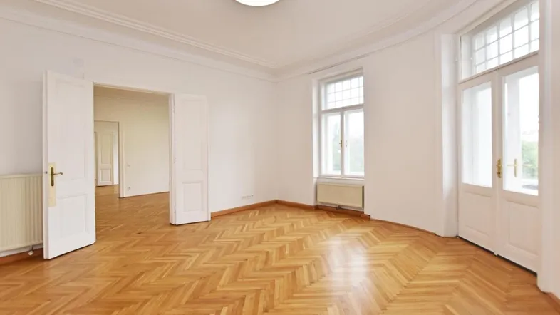 Heller Raum mit Fischgrätparkett, hohen Decken und großen Fenstern, der viel natürliches Licht bietet.