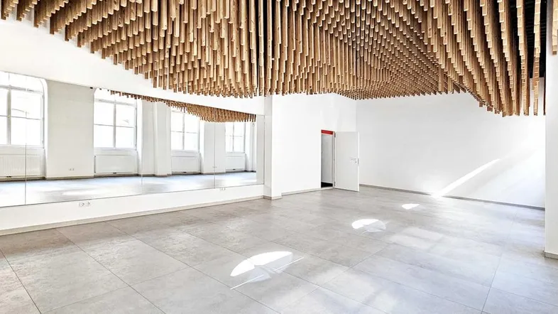 Heller, moderner Raum mit Holzlamellendecke, großen Spiegeln und Fliesenboden, ideal für Studios.