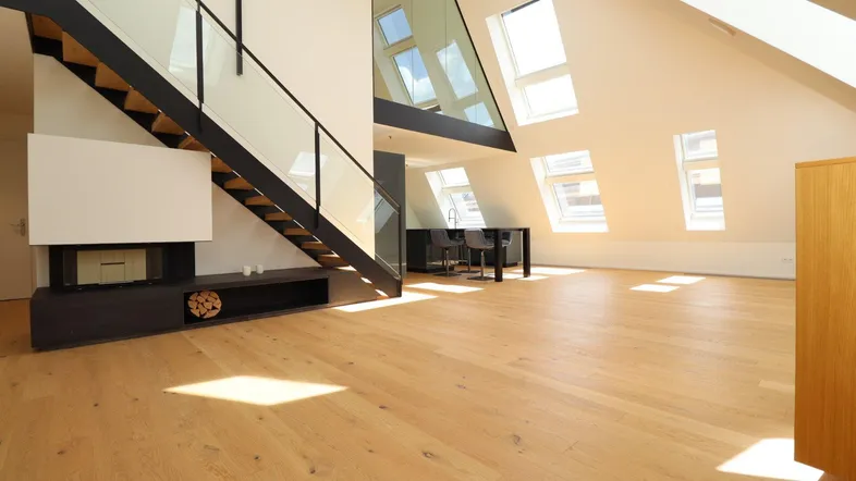 Helles, offenes Dachgeschoss mit Holzparkettboden, moderner Treppe und vielen Dachfenstern.