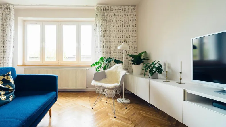 Helles Wohnzimmer mit blauem Sofa, Fischgrätparkett und großen Fenstern, modern eingerichtet.